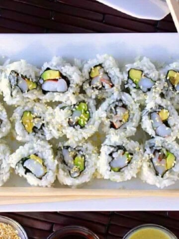 Avocado Shrimp Sushi Rolls on a white plate with chopsticks and rice.