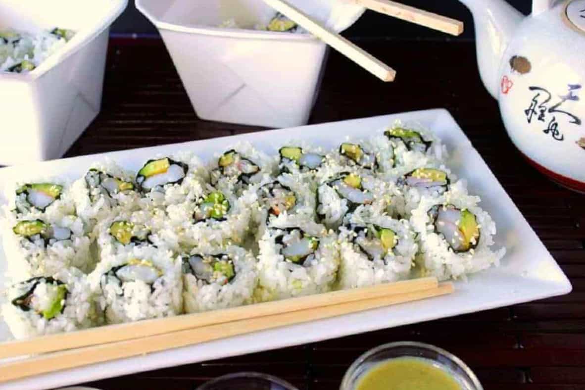 A long white tray filled with Homemade Avocado Shrimp Sushi Rolls along with some chopsticks.
