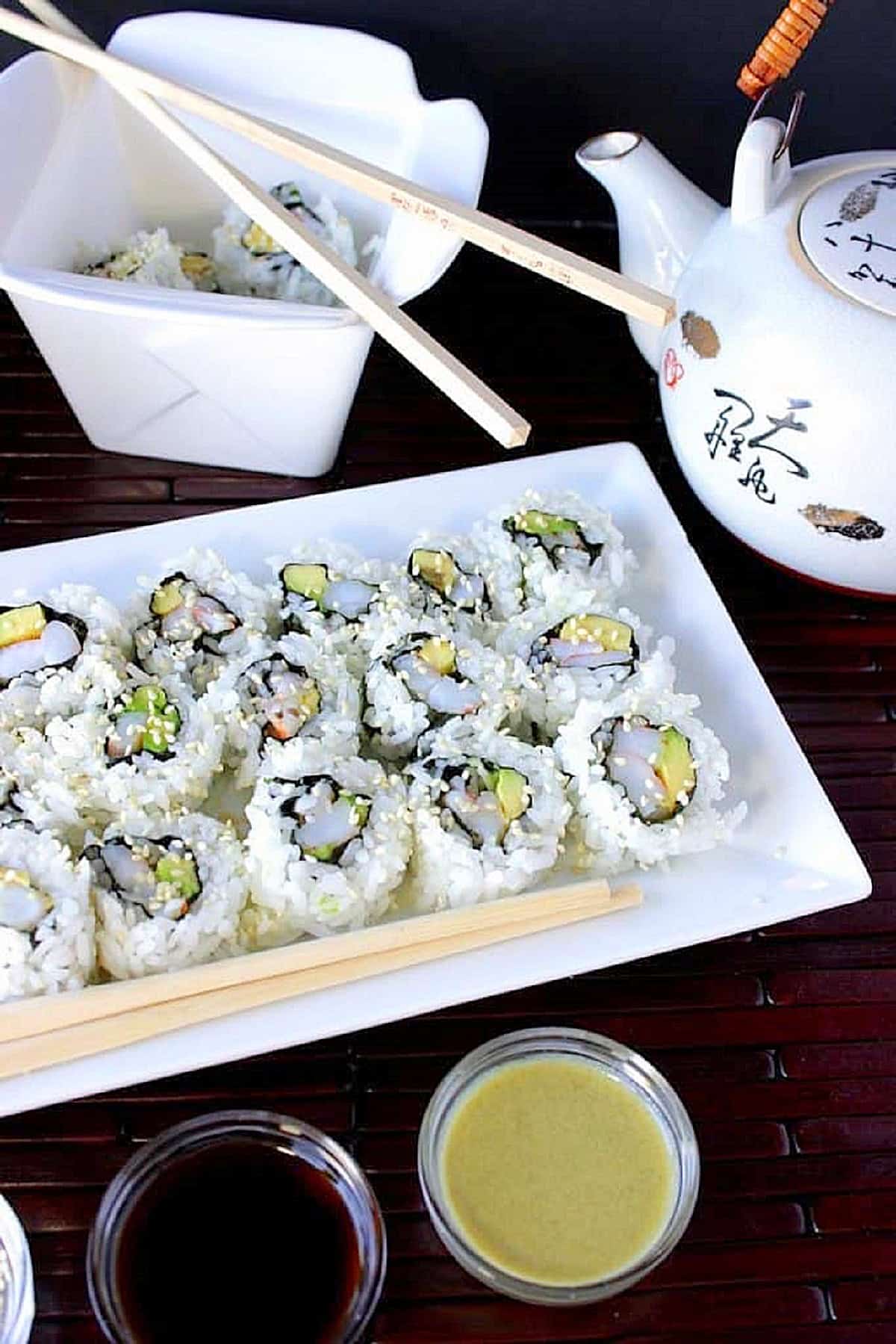 If you think that sushi rolls are only for the professionals to make, then I have a surprise for you. With the help of a few Uncommon Goods products, Homemade Avocado Shrimp Sushi Rolls come together in a snap and taste every bit as good as what you get in a restaurant. A white plate filled with avocado shrimp sushi rolls along with chopsticks and sesame seeds on the plate.