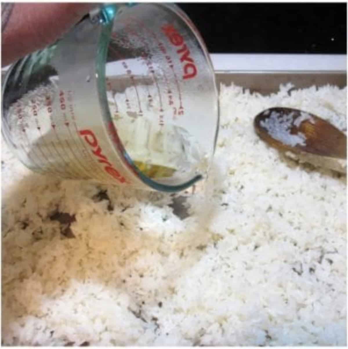 Rice wine vinegar being poured onto a baking sheet with sticky rice.
