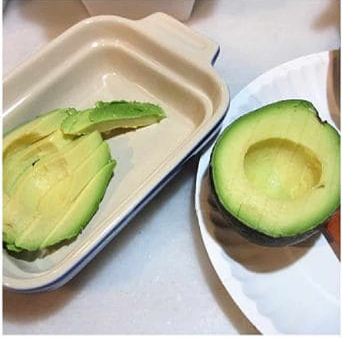 Sliced avocado in a small dish and a paper plate.