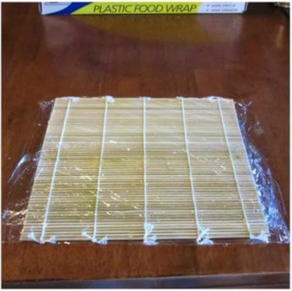 A bamboo sushi mat with plastic wrap for making homemade avocado shrimp sushi.