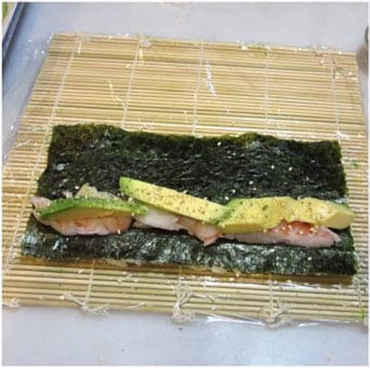 Nori, avocado, shrimp, and a sushi rolling mat making sushi rolls.