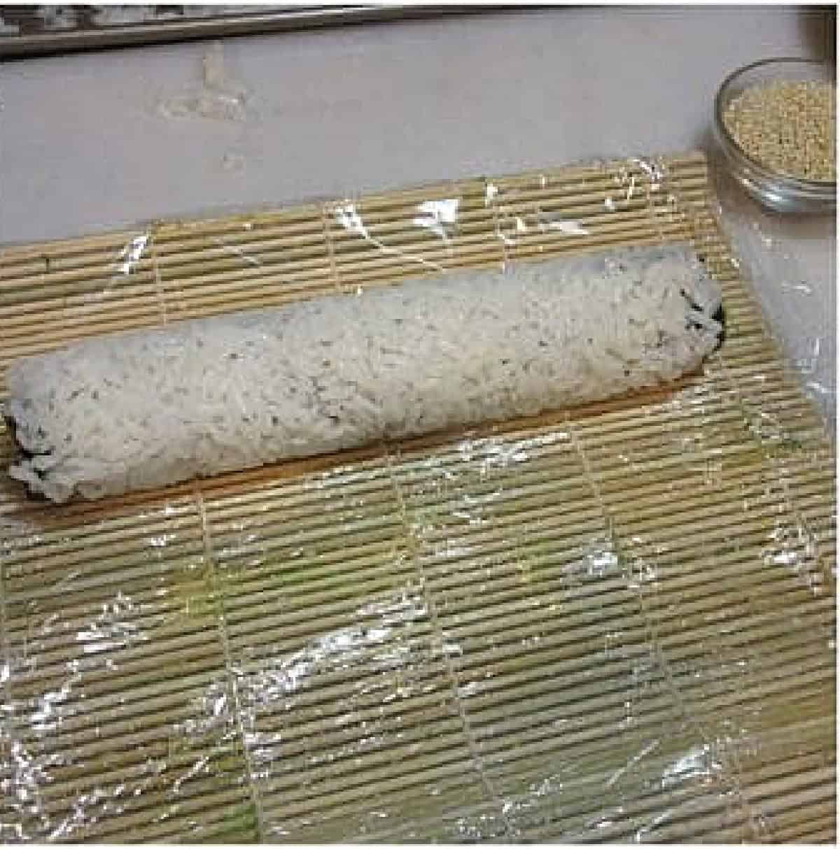 A sushi roll on a sushi mat before being sliced.