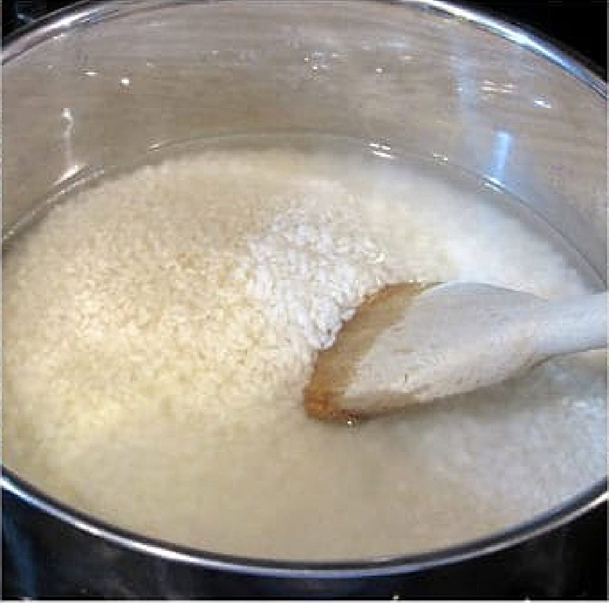 White rice in a saucepan with water and a wooden spoon.