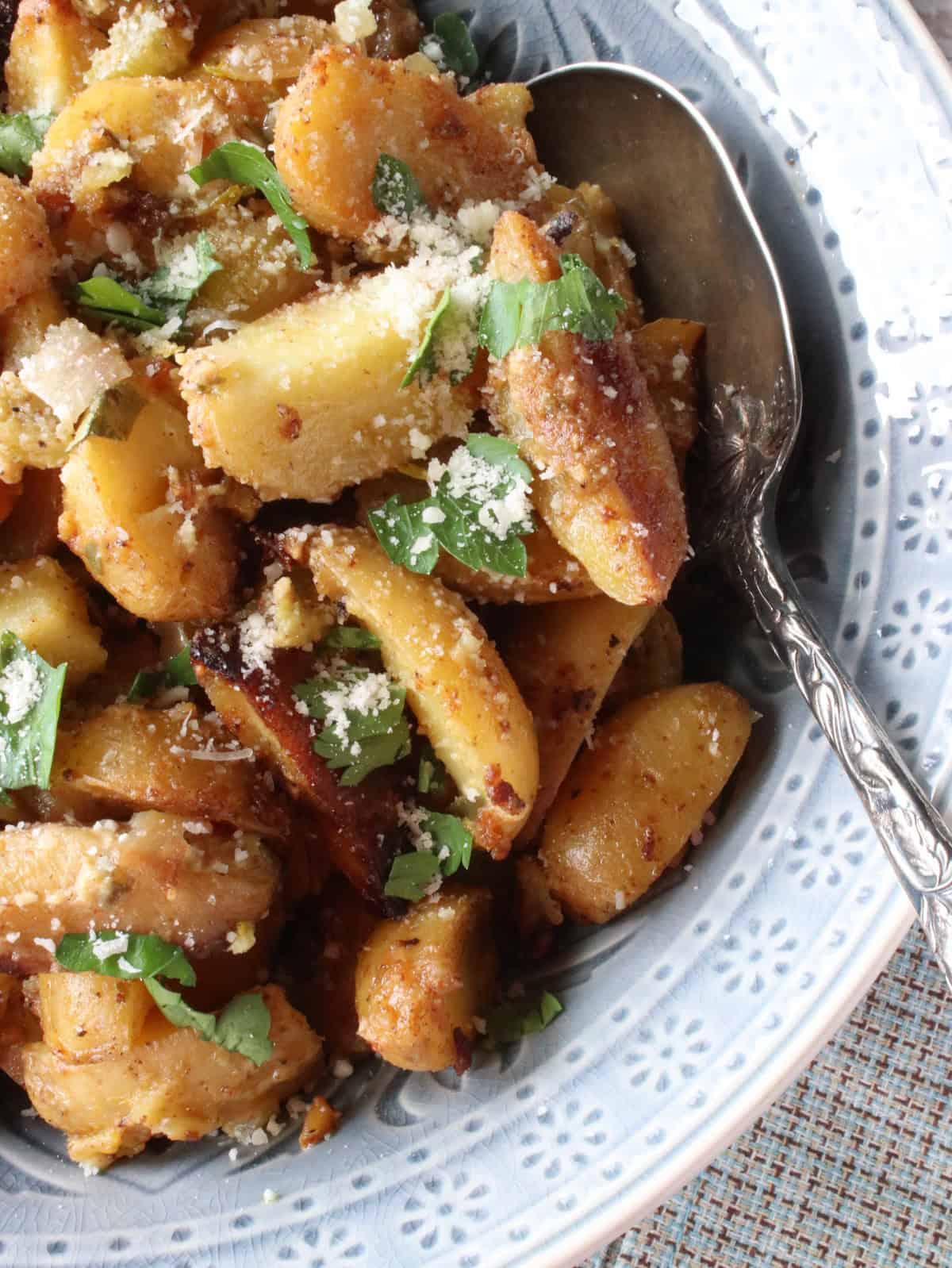Parmesan cheese on top of Hot Roasted Potato Salad in a blue bowl.