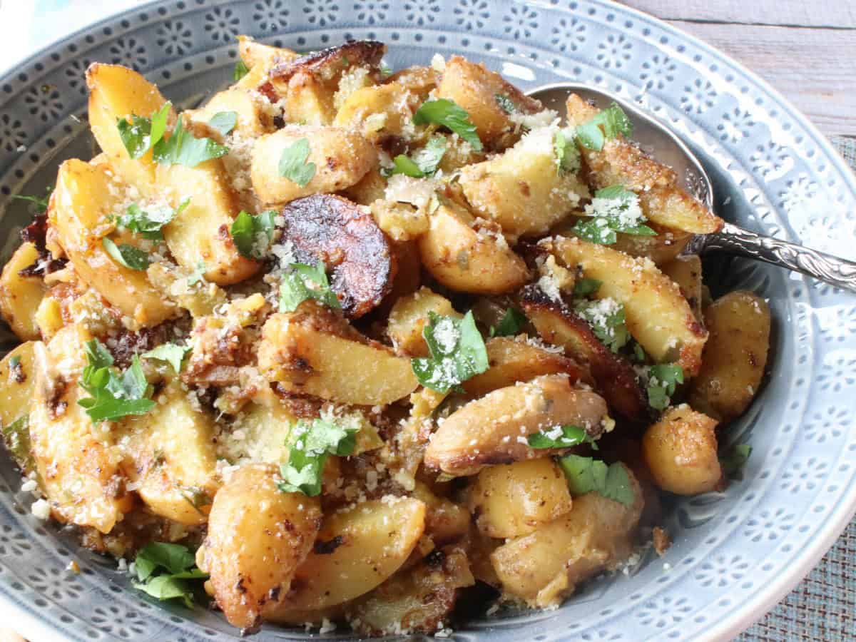 Celery leaves and Parmesan cheese on top of Hot Roasted Potato salad in a bowl.