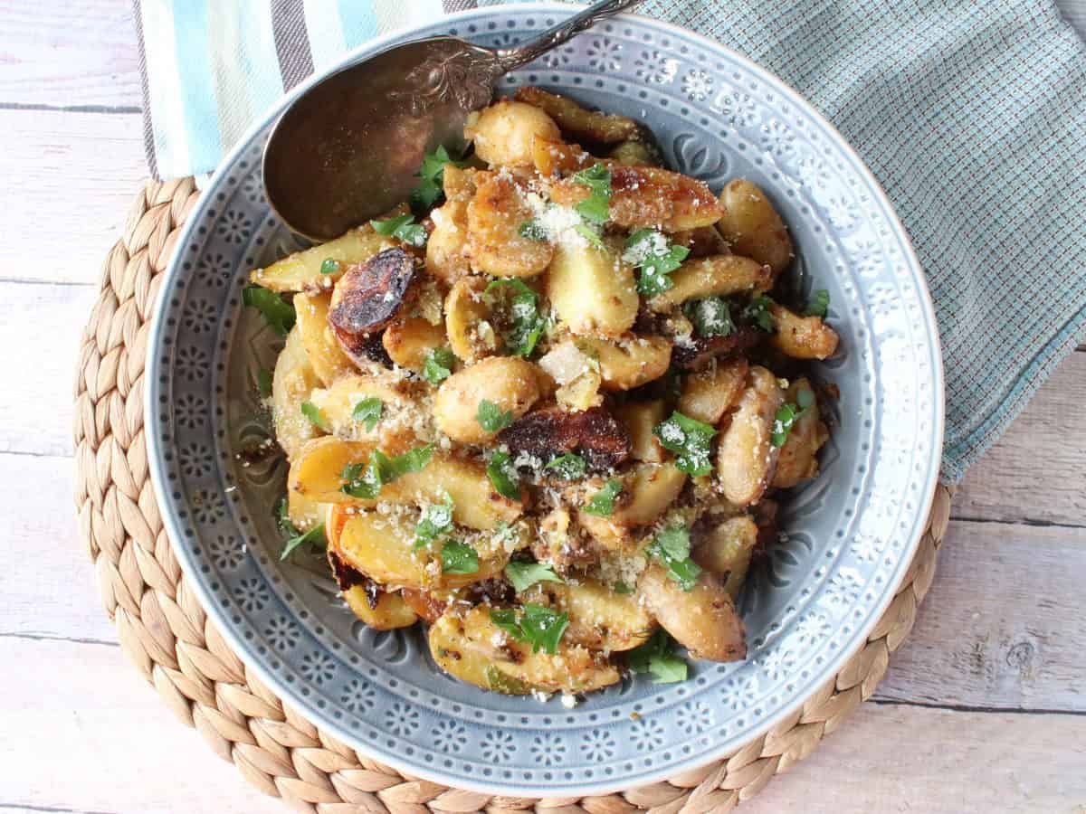 A blue bowl with blue napkins along with plenty of Roasted Potato Salad topped with cheese and greens.