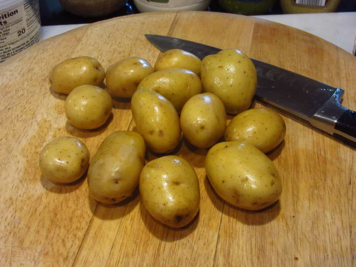 Washed baby Yukon potatoes on a cutting board with a knife.