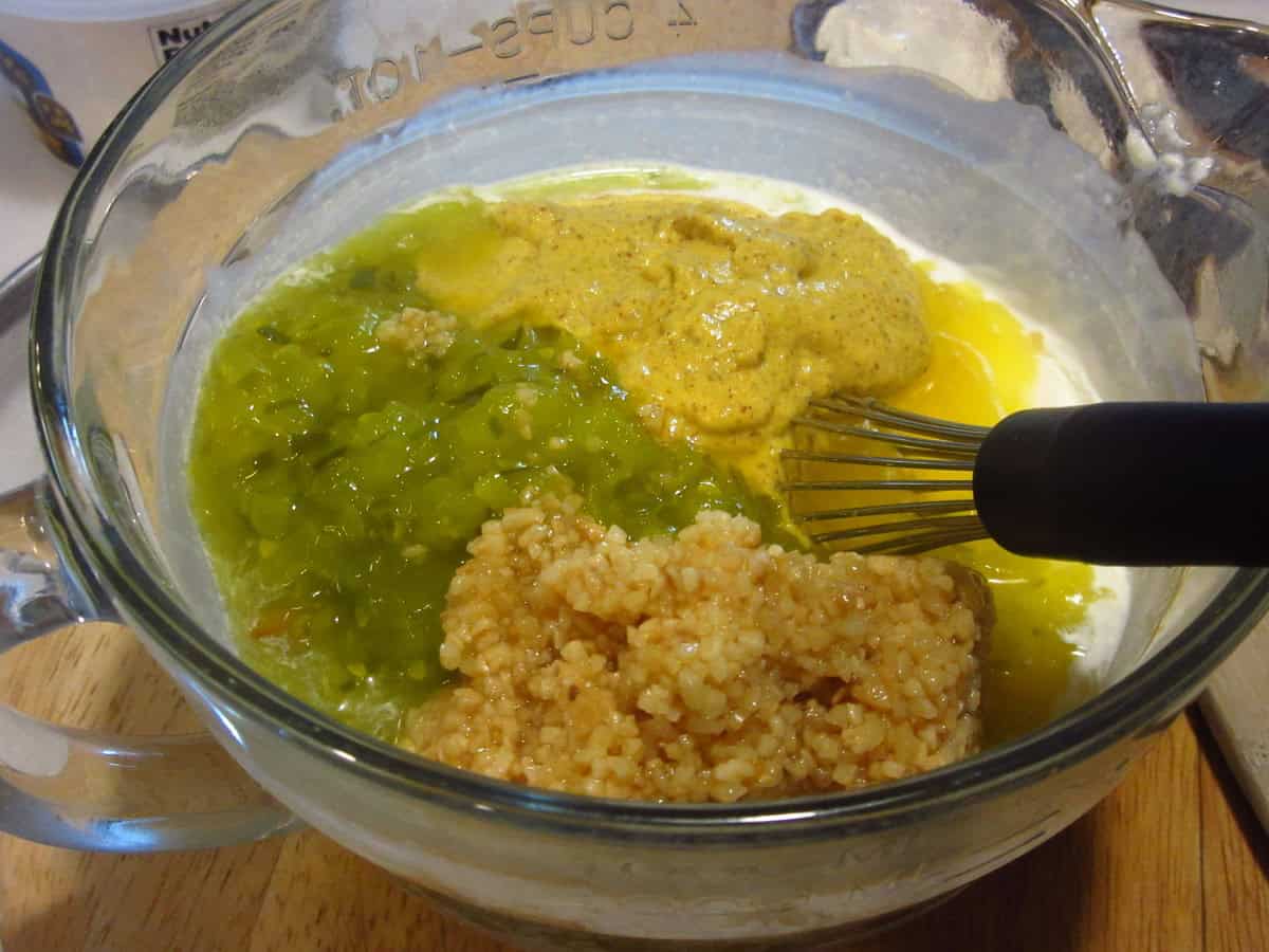 Relish, garlic, mustard, and mayo in a glass measuring cup making a sauce for hot roasted potato salad.