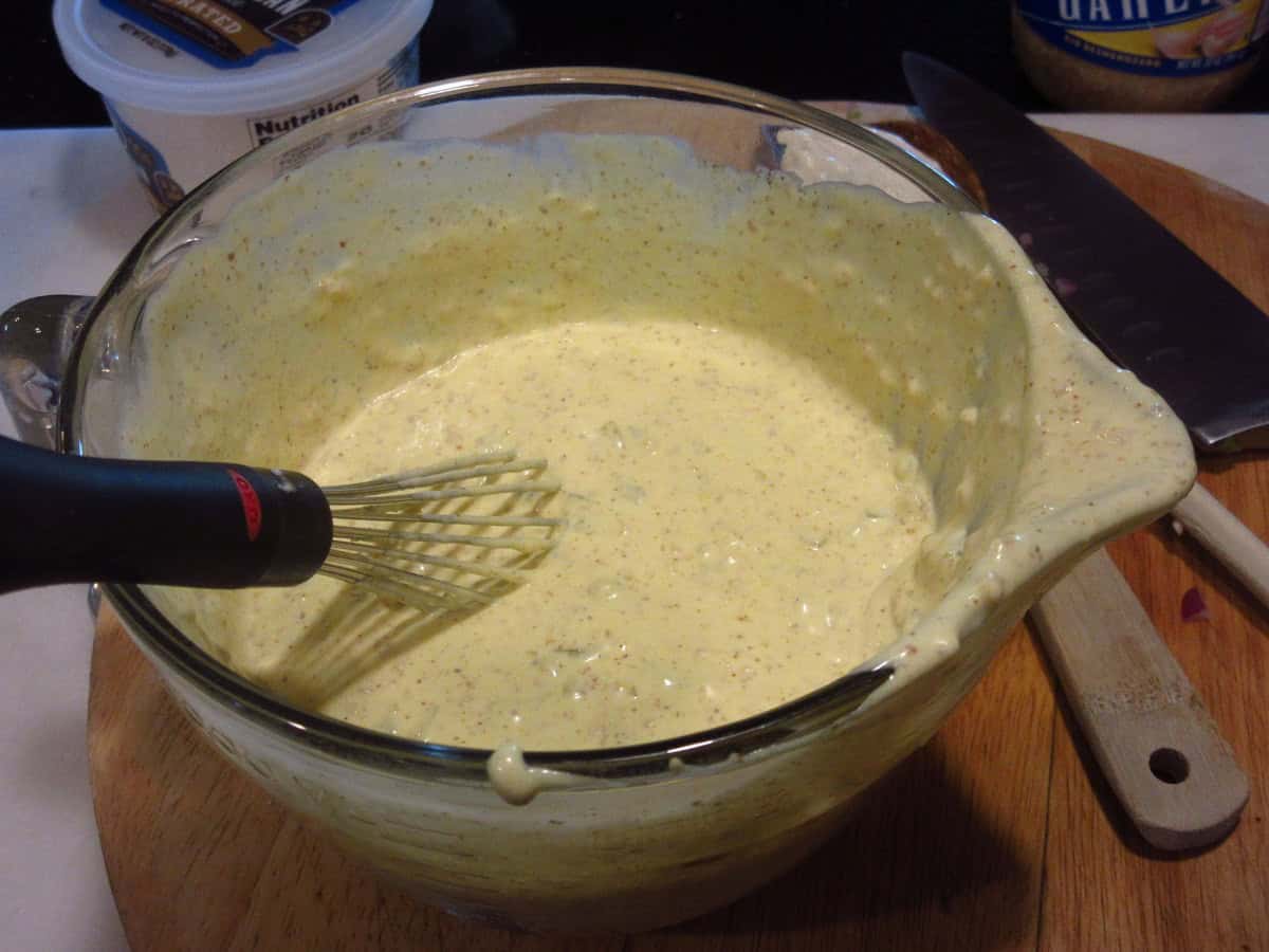 A creamy dressing in a glass measuring cup with a whisk for hot roasted potato salad.