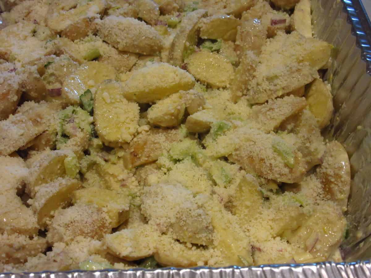 Grated Parmesan cheese sprinkled over cut baby Yukon potatoes in a baking pan.