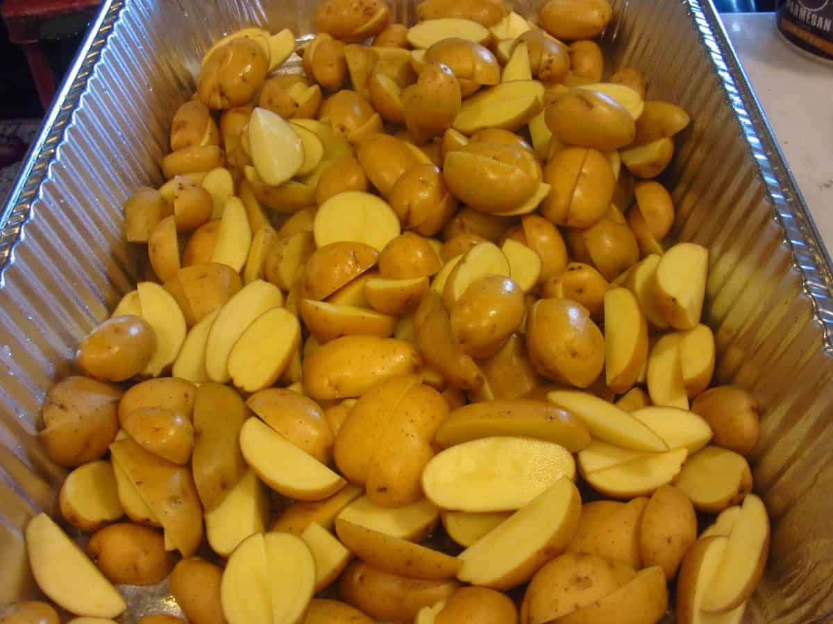 Cut up baby Yukon potatoes in a silver disposable roasting pan.