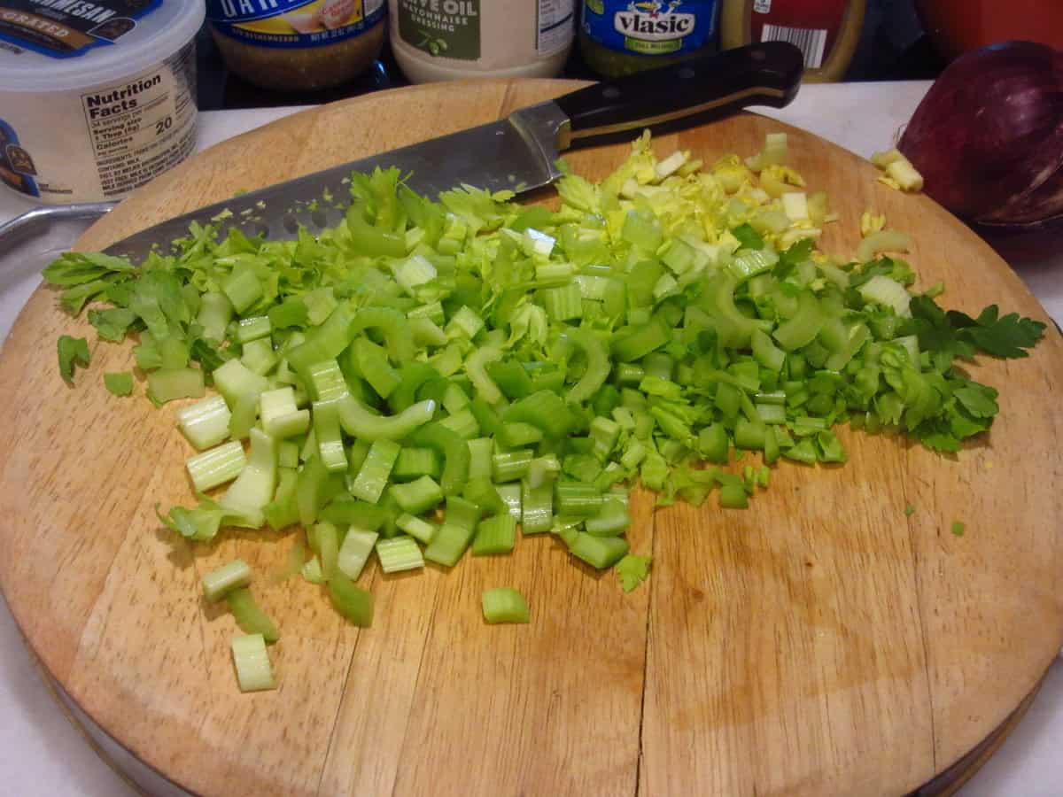 Diced celery and celery leaves on a wooden cutting board with a knife.