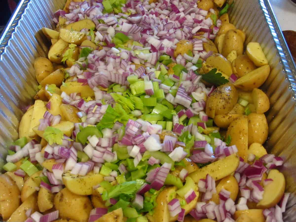 Raw cut up baby Yukon potatoes in a roasting pan with onions and chopped celery.