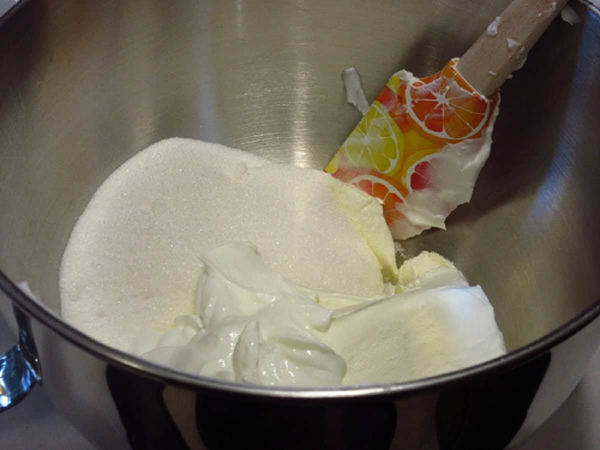 Cream cheese, sour cream, and sugar in a stainless steel mixing bowl.