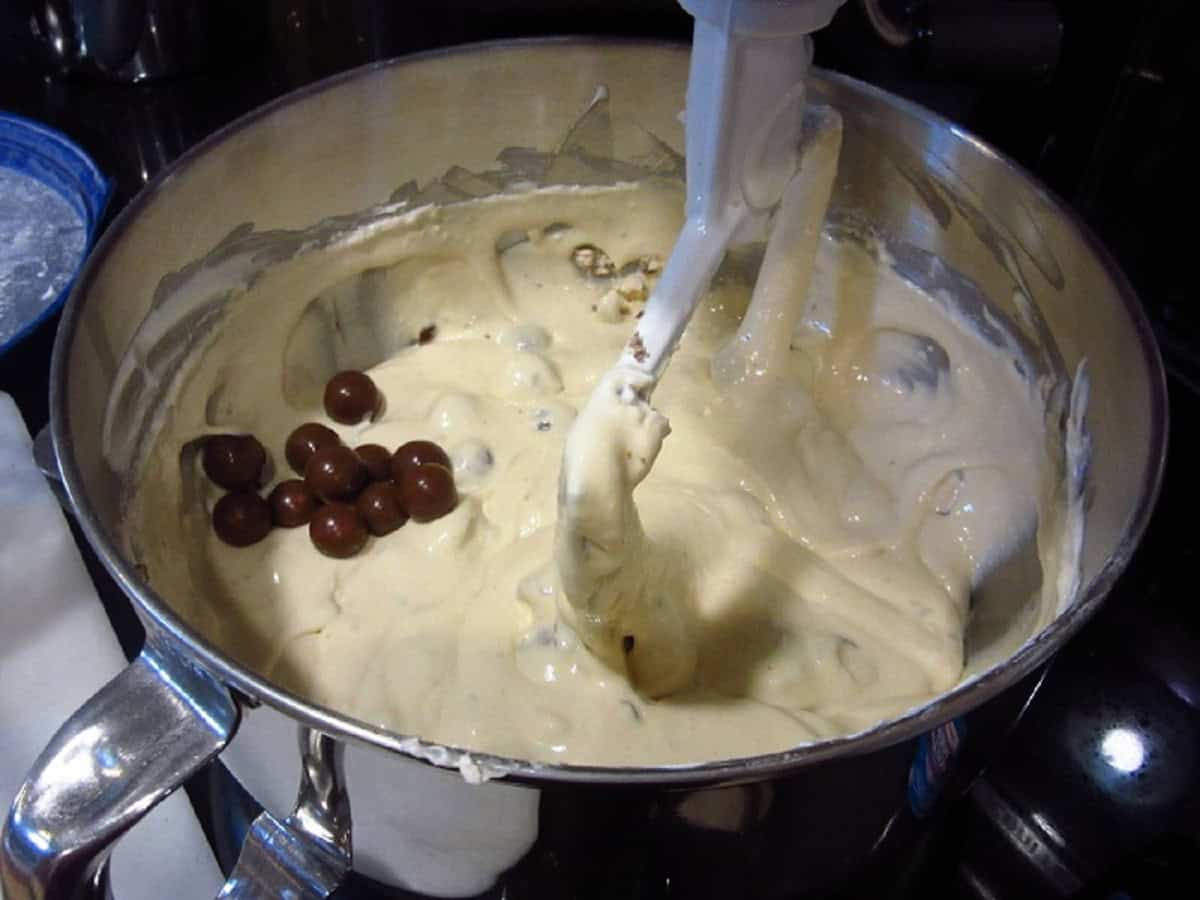 A cheesecake batter in a stand mixer with whoppers malted milk balls.