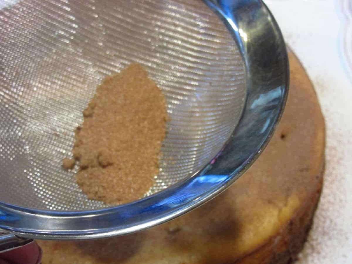 Malted milk ball powder in a strainer over a cake.