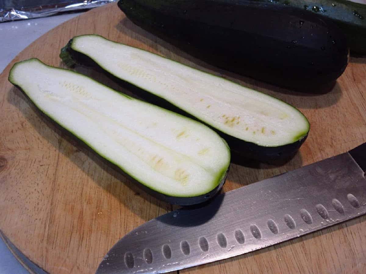 A halved zucchini on a cutting board with a knife.