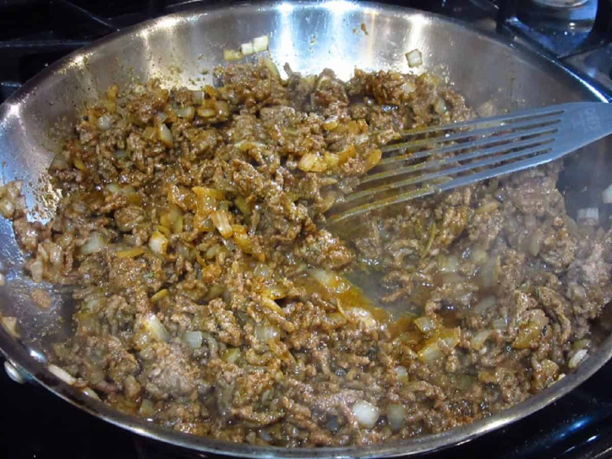 Ground beef, onions, and taco seasoning in a large skillet with a slotted spatula.