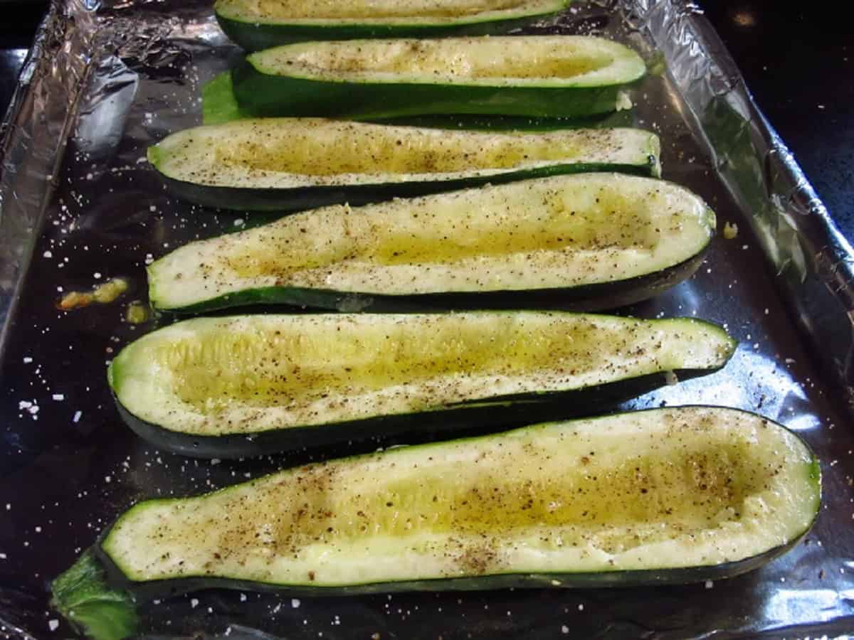 Hollowed zucchini with oil salt and pepper on a baking sheet.