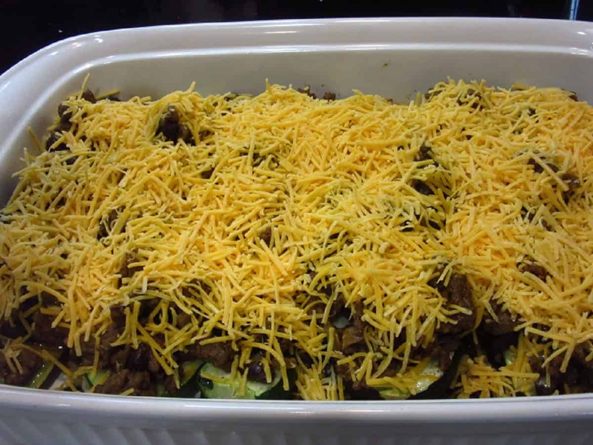 Shredded cheddar cheese on top of ground beef for making taco zucchini boats.