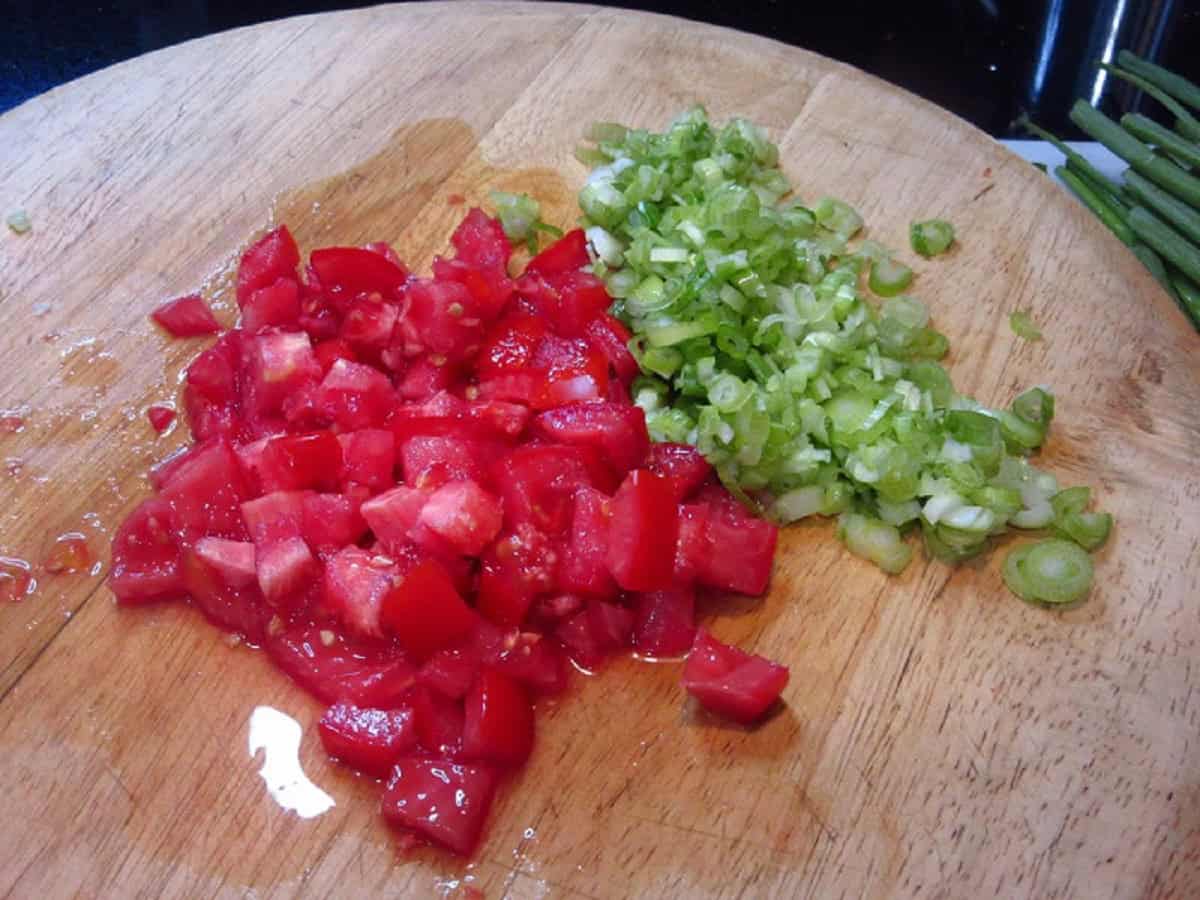 Chopped tomato and scallions on a wooden cutting board.
