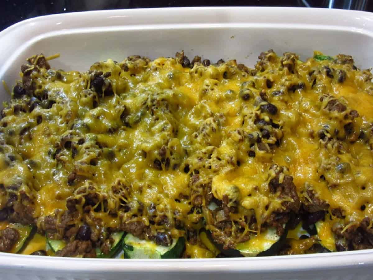 Melted cheese over ground beef taco zucchini boats in a white casserole dish.