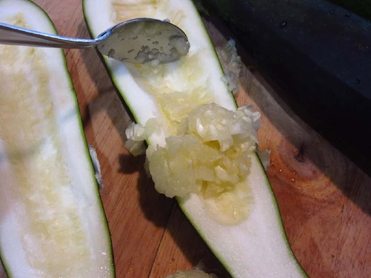 A spoon scraping out the seeds from a halved zucchini.