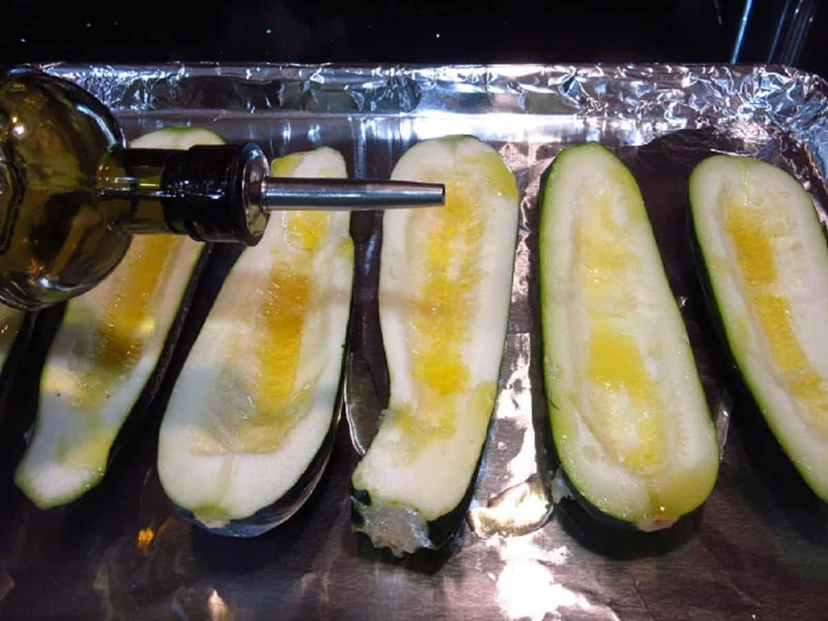 An oil bottle drizzling oil onto halved zucchini.