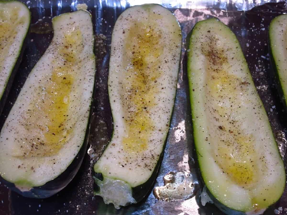 Zucchini boats with oil, salt and pepper on a tin foil covered baking sheet.