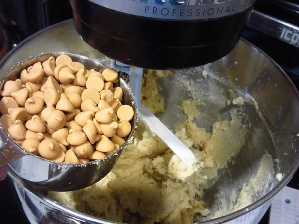 Peanut butter chips being added to a stand mixer bowl.