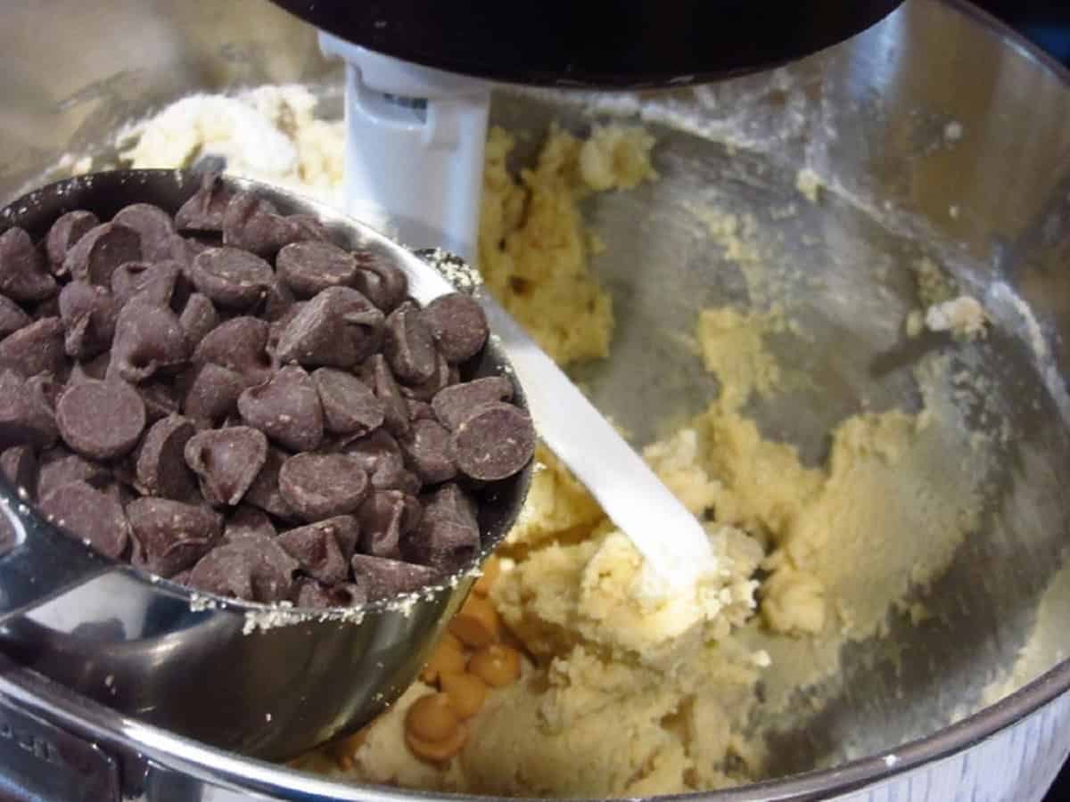 Chocolate chips in a measuring cup being added to a cookie dough.