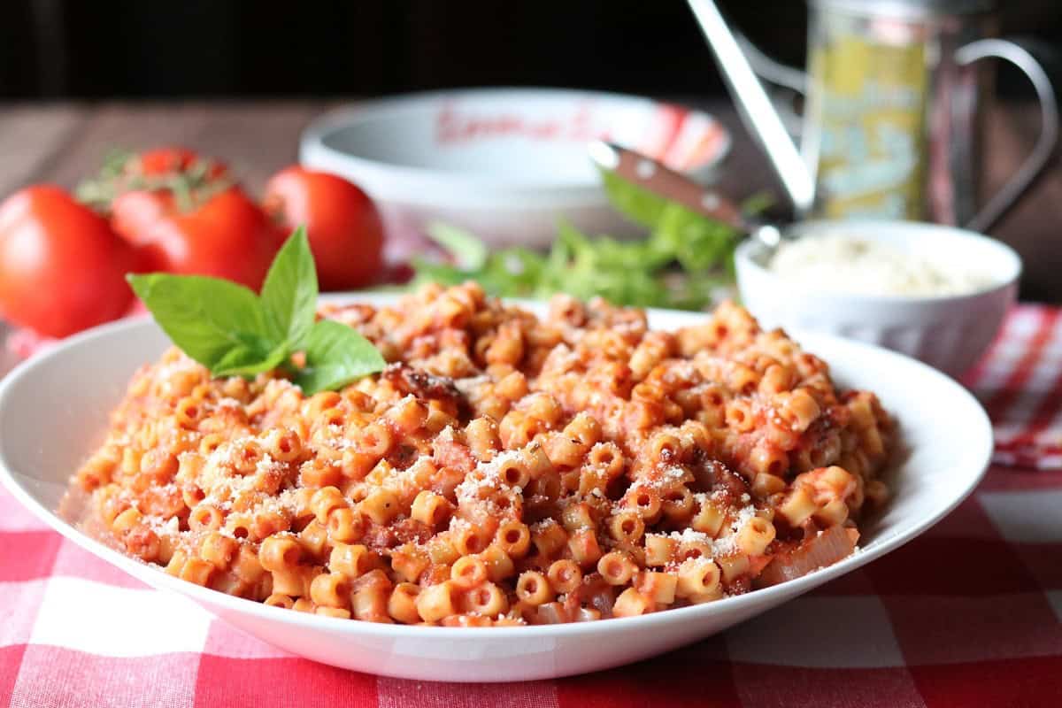 A Italian ditallini pasta dinner with tomatoes, basil, and olive oil in the background.