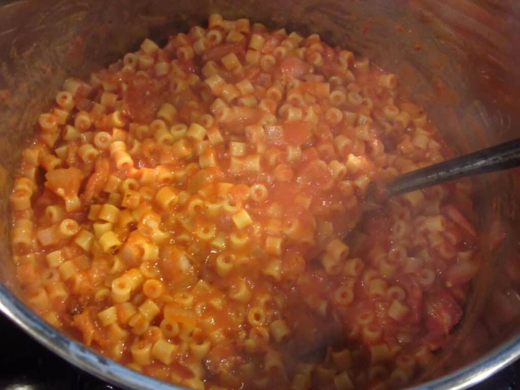 A large pasta pot with tomato bacon pasta with mascarpone sauce and a metal spatula.