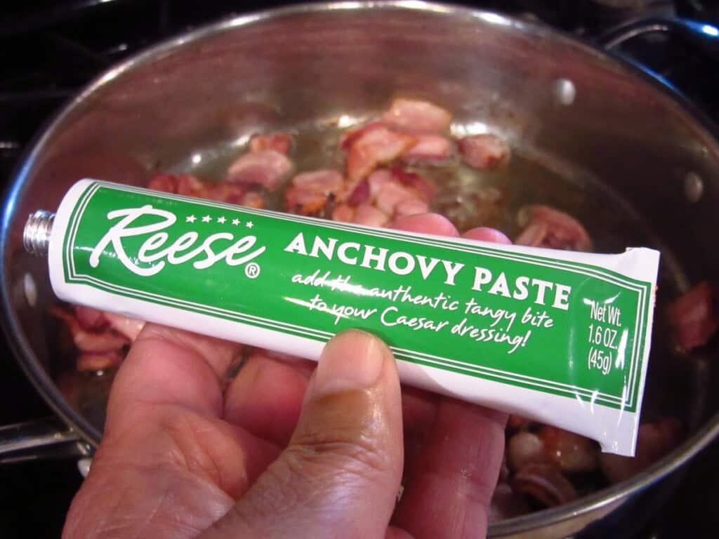 A hand holding a tube of anchovy paste.