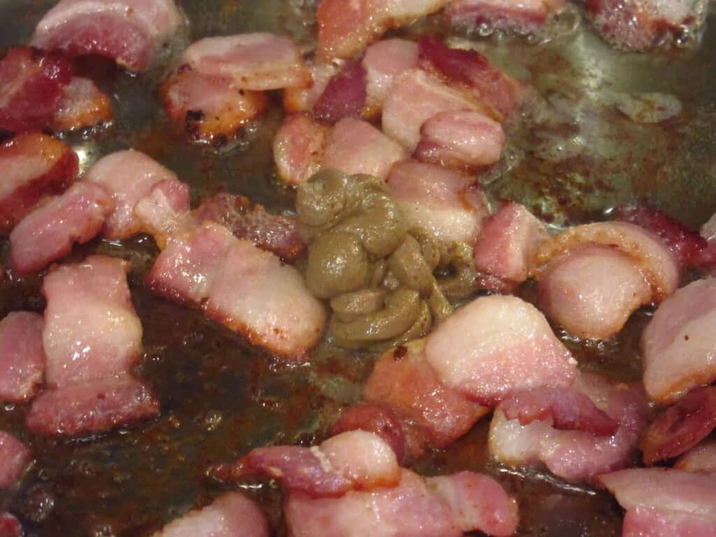 Anchovy paste and cut up bacon browning in a skillet.
