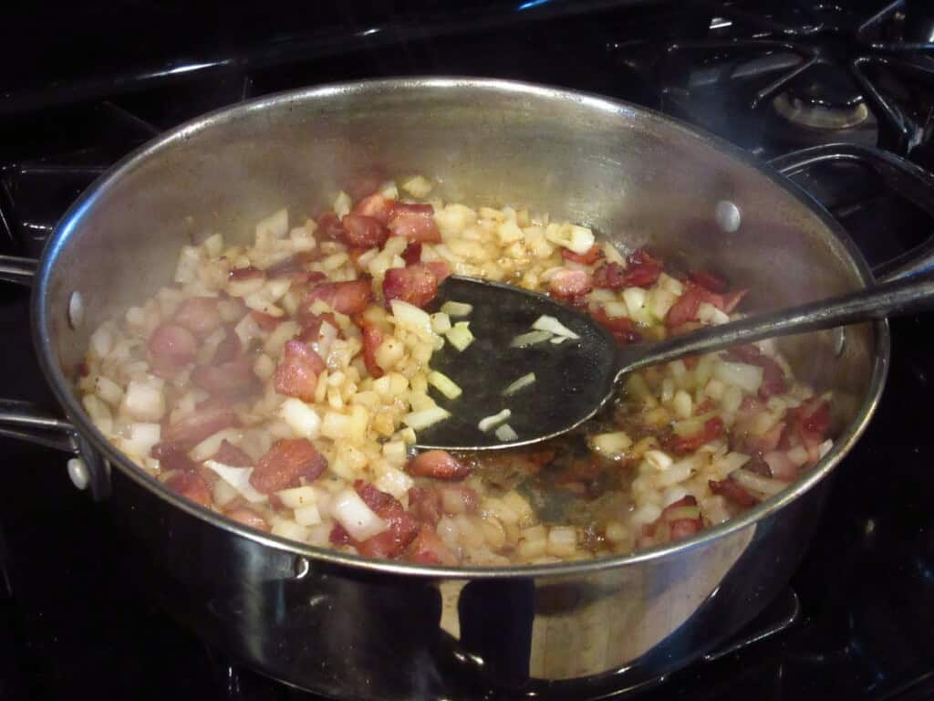 A metal spatula in a large skillet with bacon and onions.