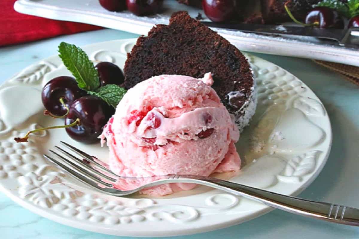 A white plate with a pink scoop of cherry amaretto ice cream and a slice of chocolate cake.