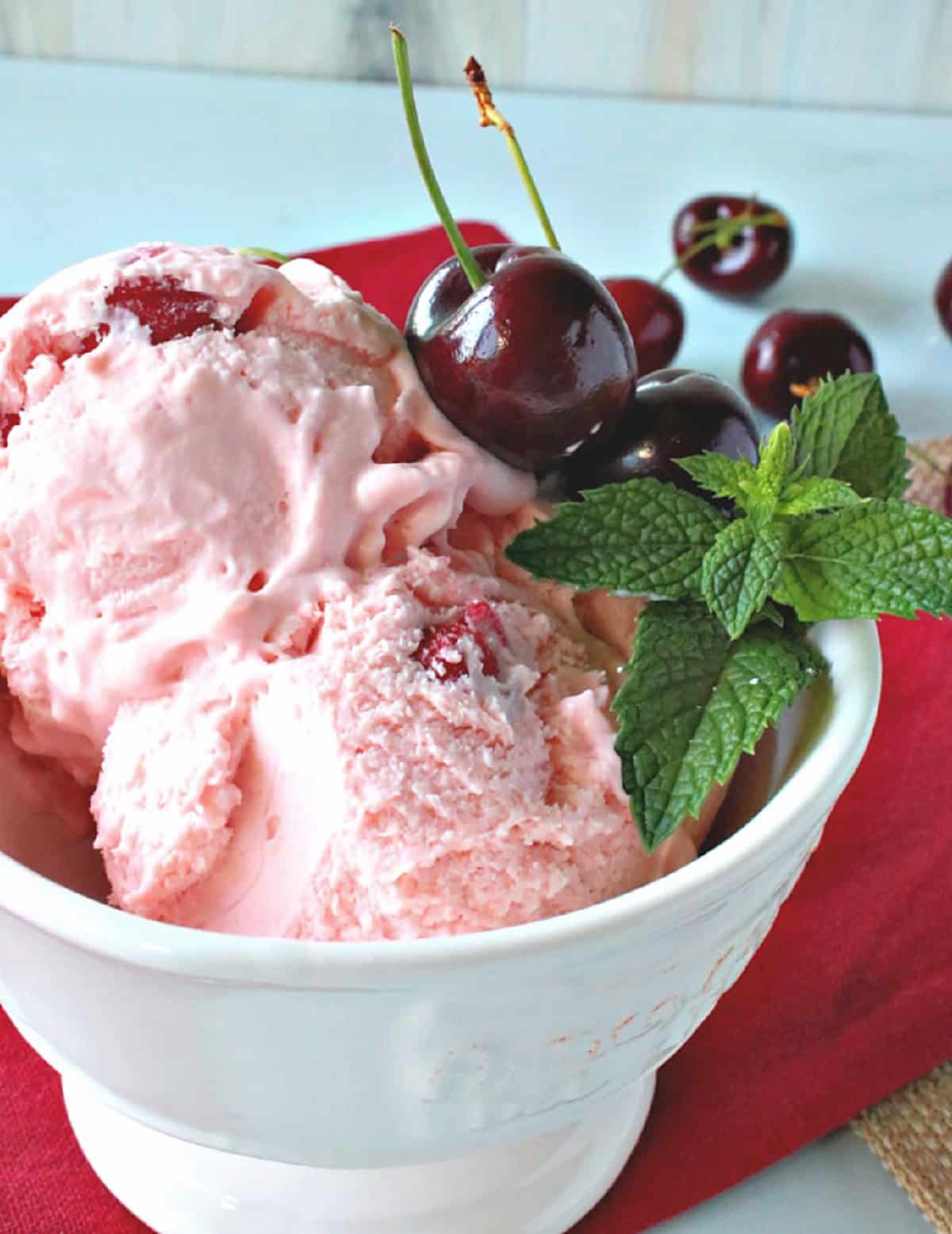 A small white dish of cherry amaretto ice cream with fresh mint as garnish.