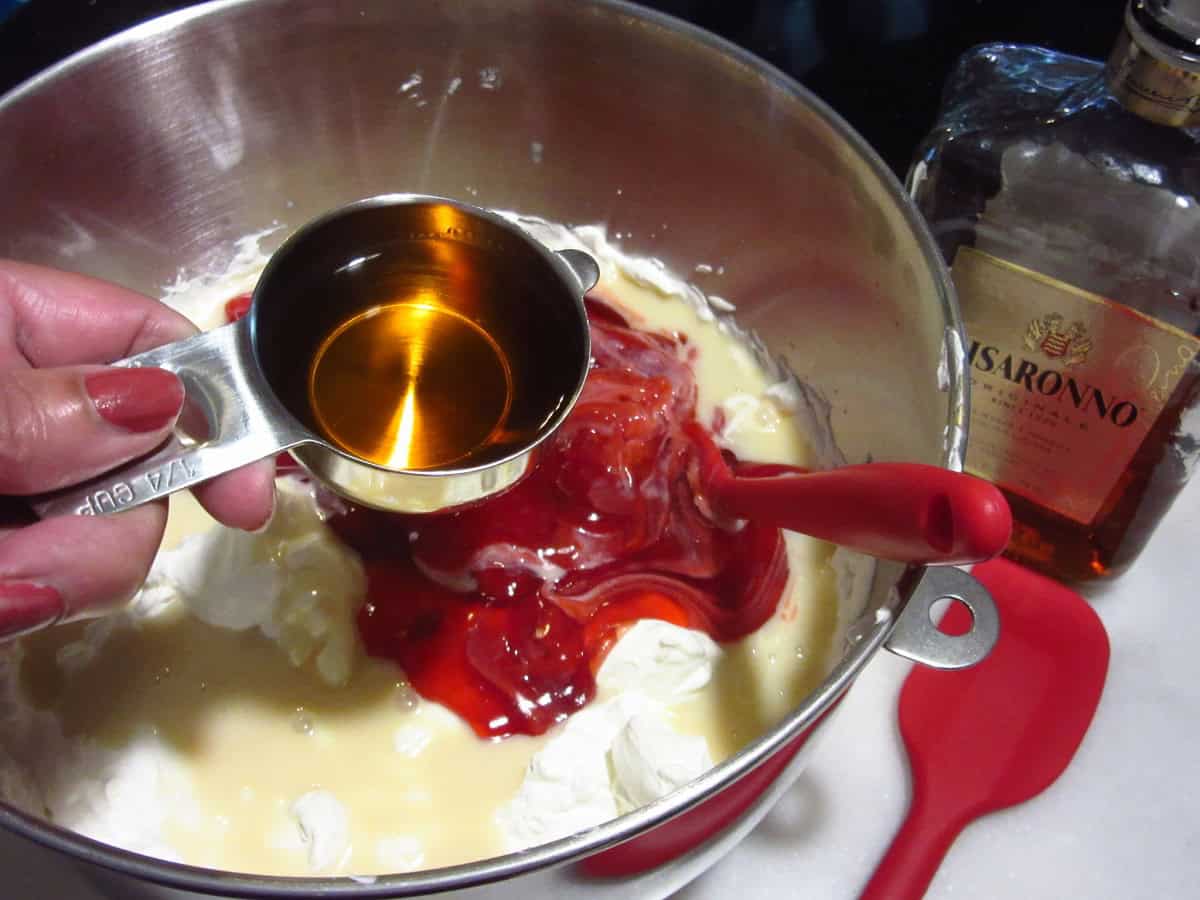 Amaretto in a measuring cup being added to a no-churn cherry ice cream base.