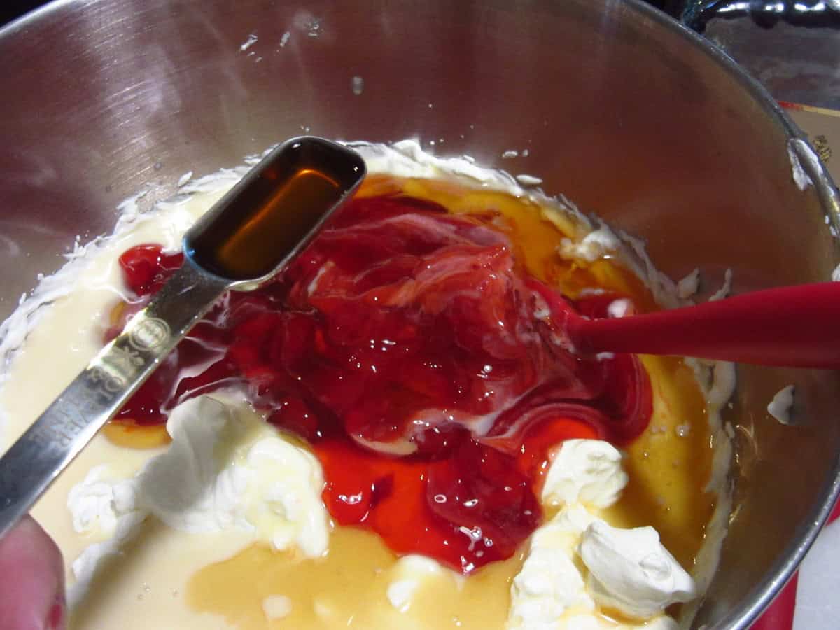 Vanilla extract in a measuring spoon being added to a cherry ice cream base.