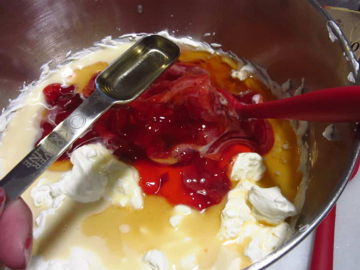 Almond extract in a measuring spoon being added to a cherry ice cream base.