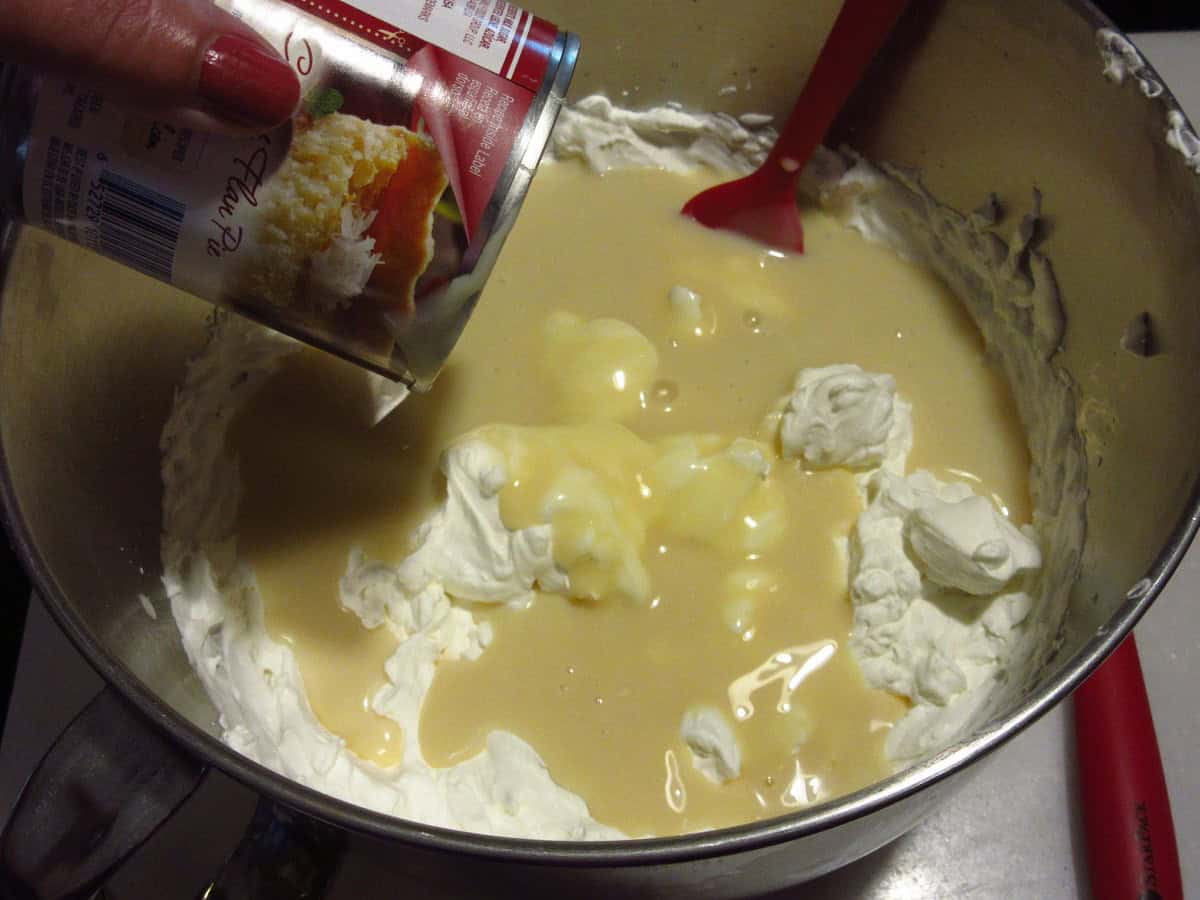 Sweetened condensed milk poured into a bowl of whipped cream.