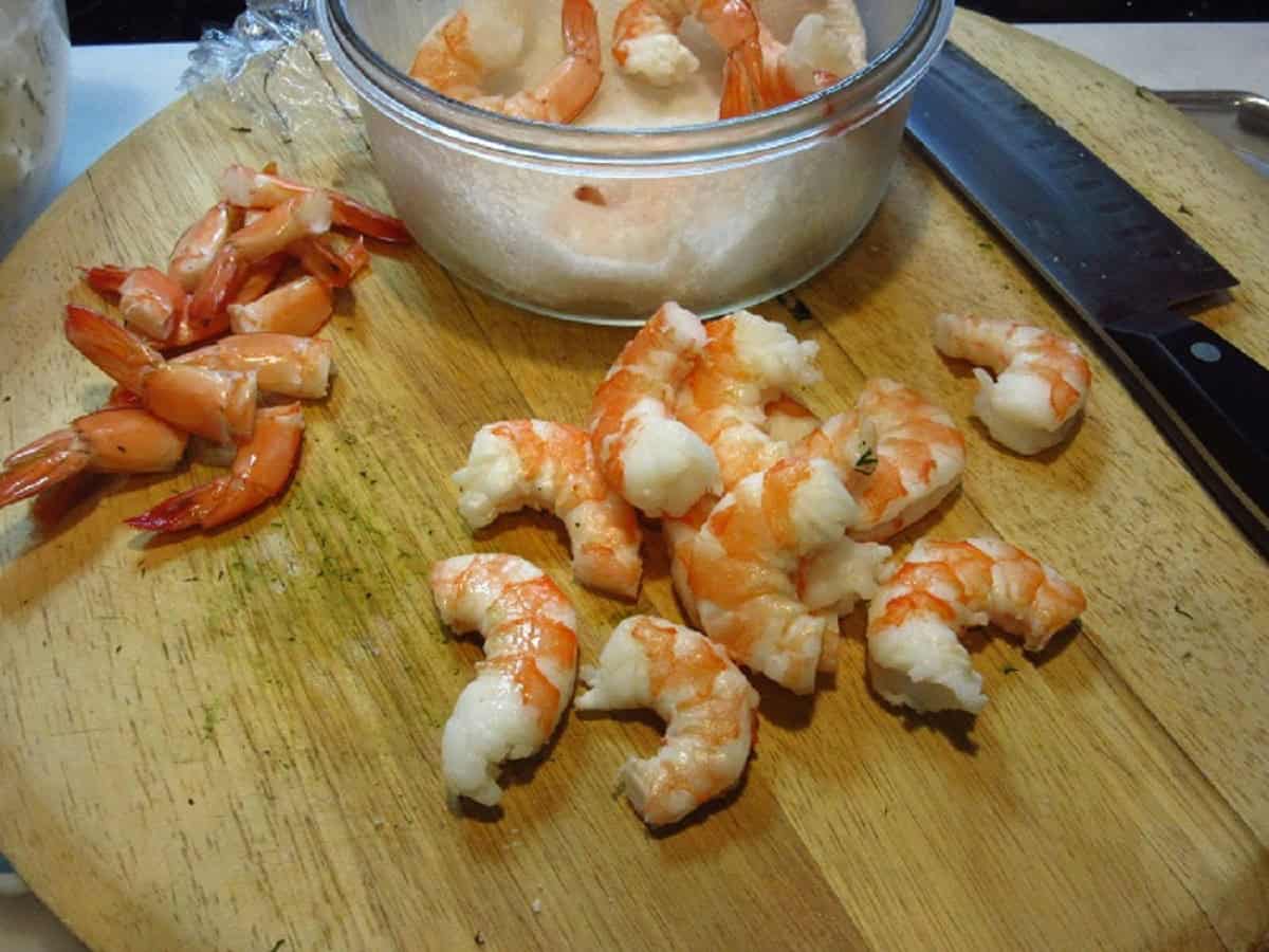 Cooked shrimp without tails on a cutting board.