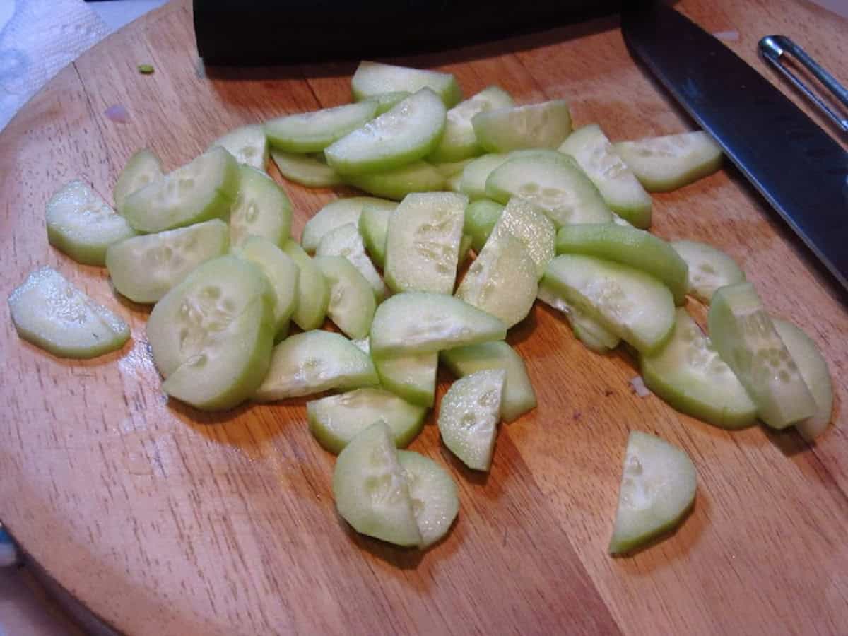 Fresh sliced and peeled cucumbers on a wooden cutting board.