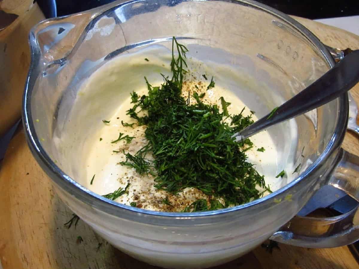 Fresh dill added to a creamy sauce in a measuring cup.