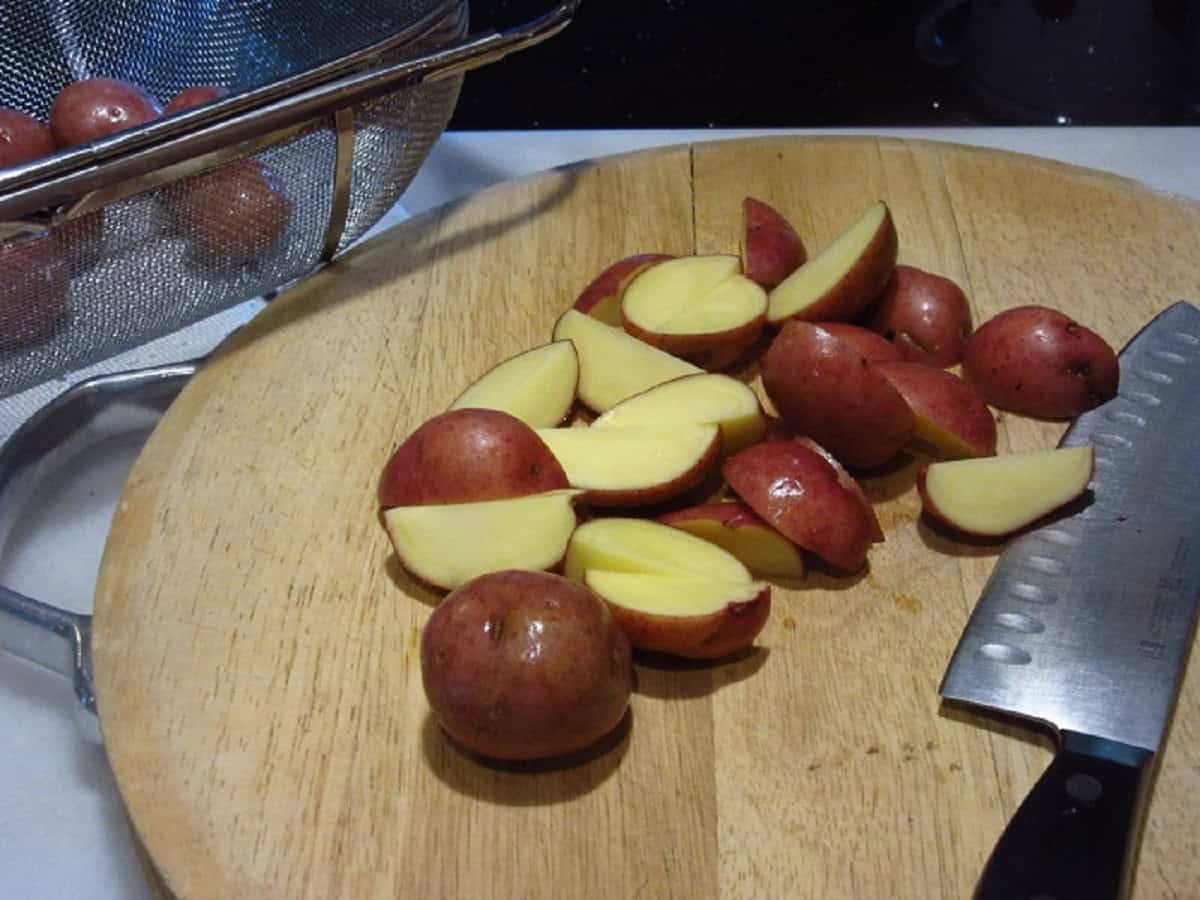 Baby red potatoes on a wooden cutting board with a knife.