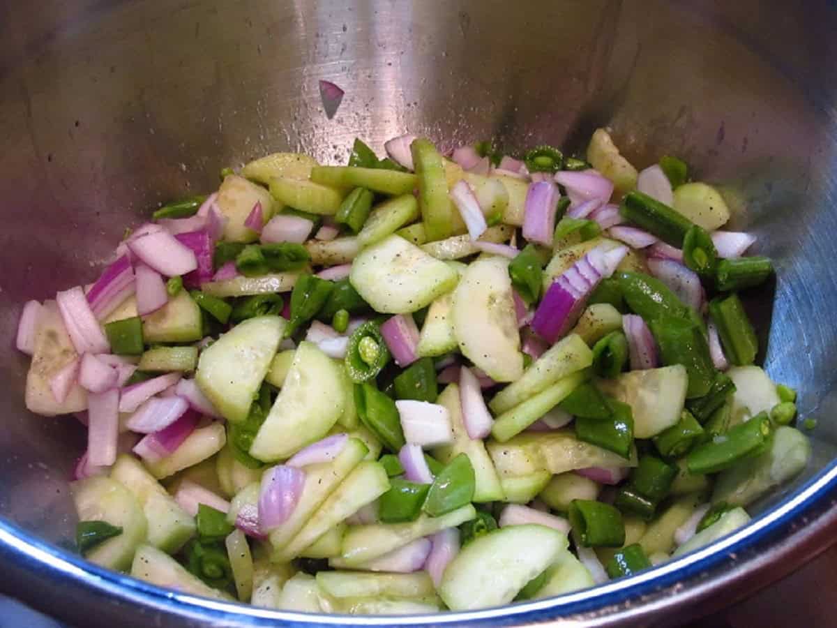 Cucumbers, snap peas, and red onion in a stainless bowl.