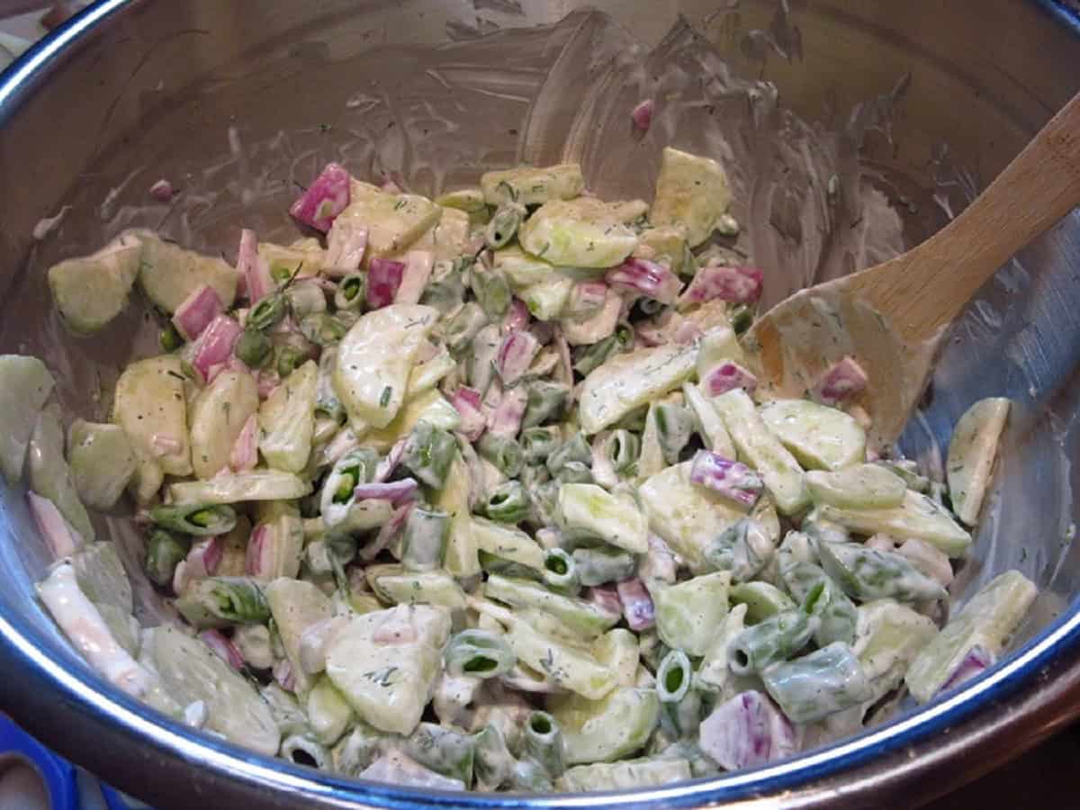 A stirred shrimp and cucumber salad in a stainless bowl with a wooden spoon.
